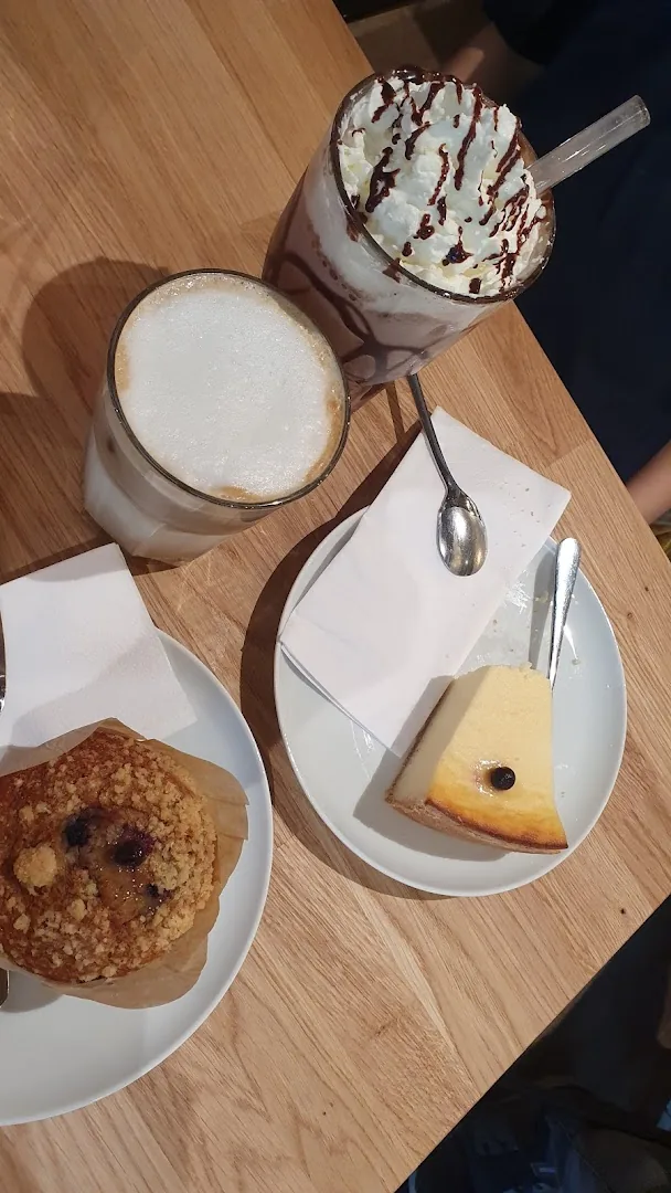 Latte Macchiato, Eisschokolade, Muffin und Cheesecake auf einem Holztisch