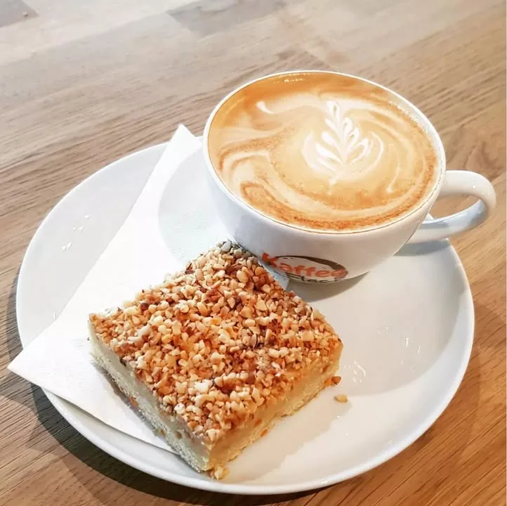 Cappuccino mit Latte-Art und eine Nussecke auf einem Teller