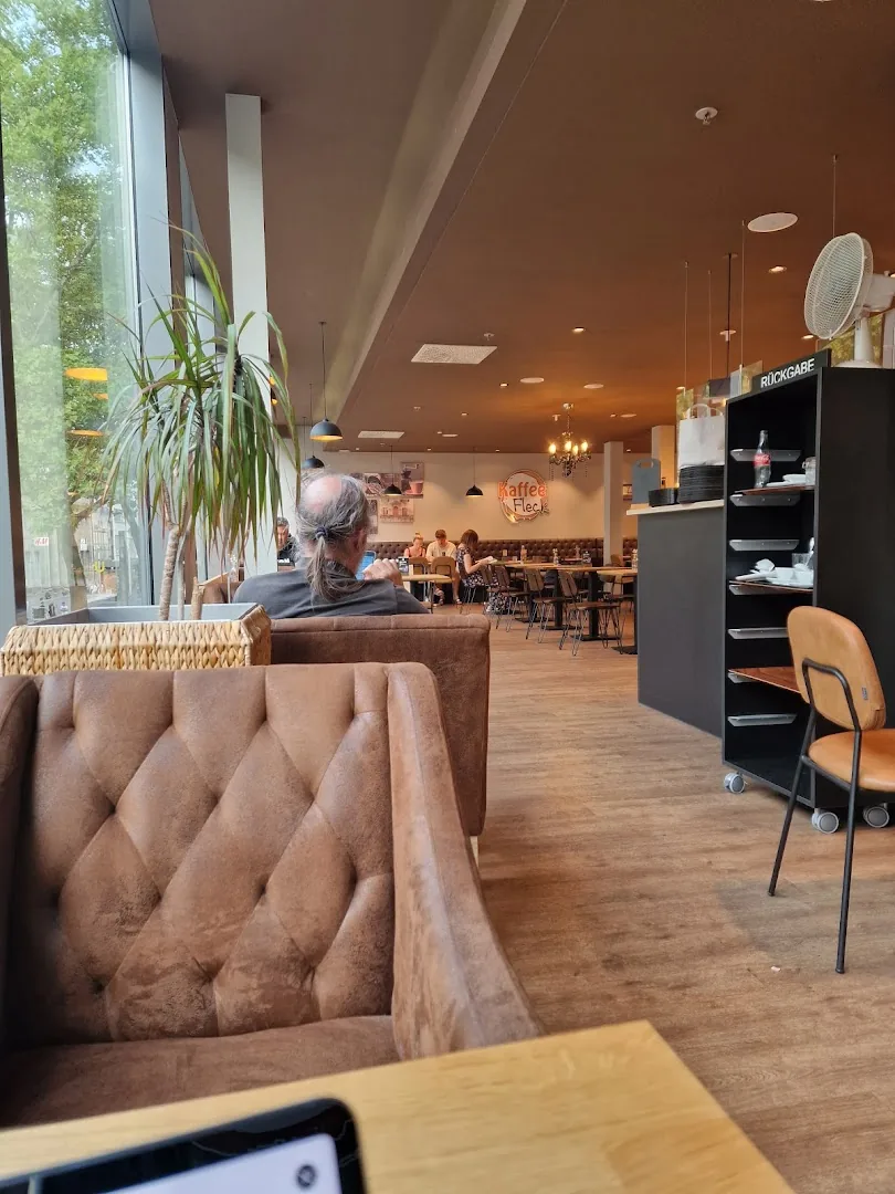 Gemütlicher Innenraum von Kaffee Fleck mit braunen Ledersesseln, Holzboden und Fensterfront zur Kaiserstraße
